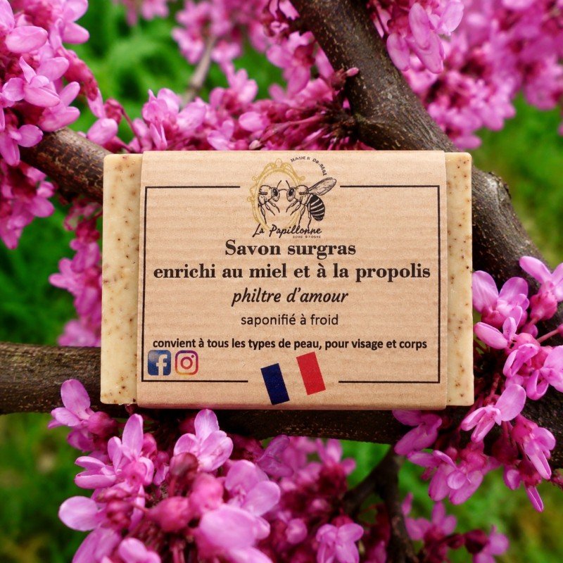Savon artisanal enveloppé dans une étiquette beige posé sur des branches fleuries roses.